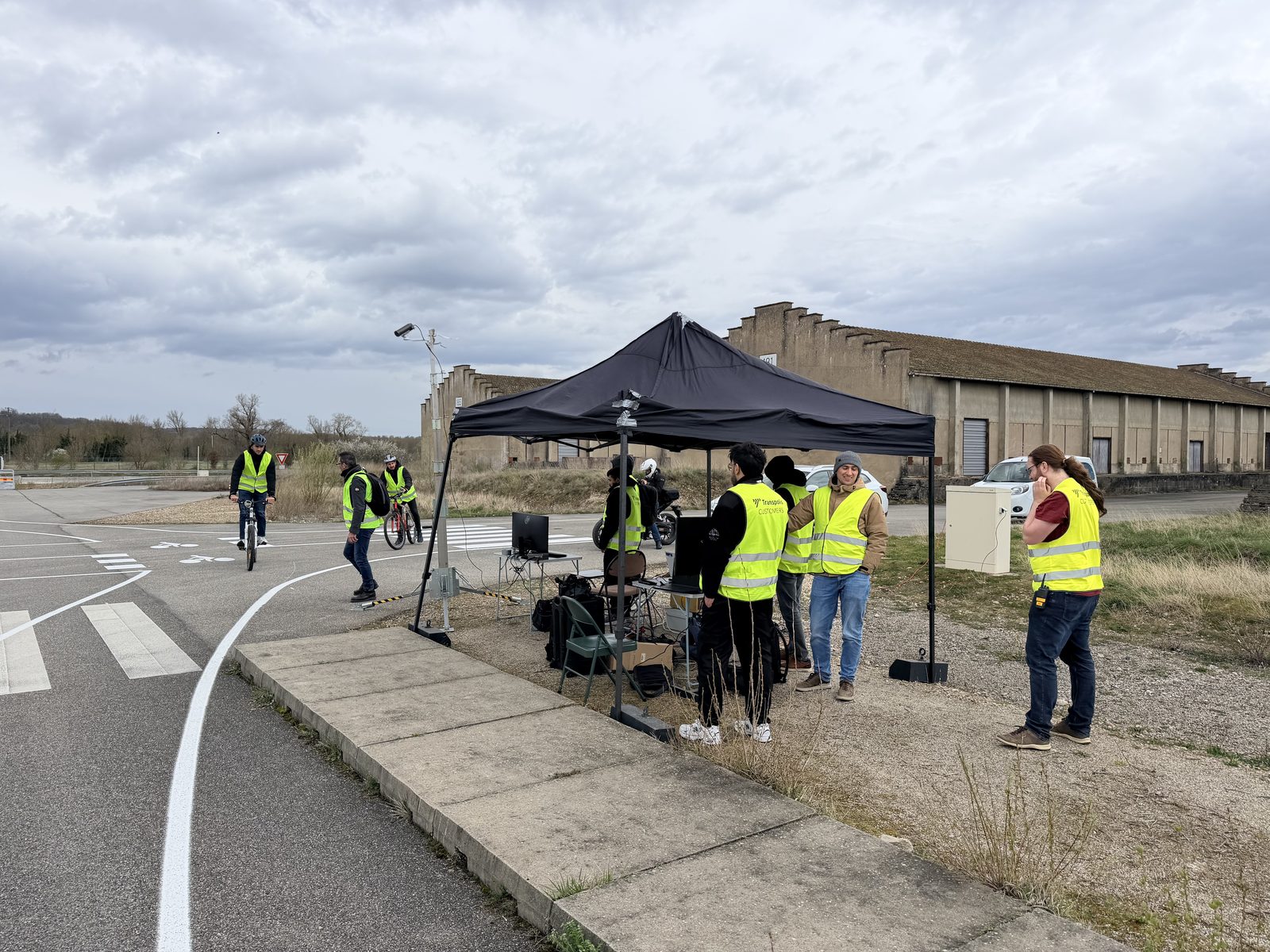 The iDriving pilot set-up at the Transpolis test track: a control tent with monitors next to a test intersection with cycle lanes and a zebra crossing, with cyclists in high-visibility vests