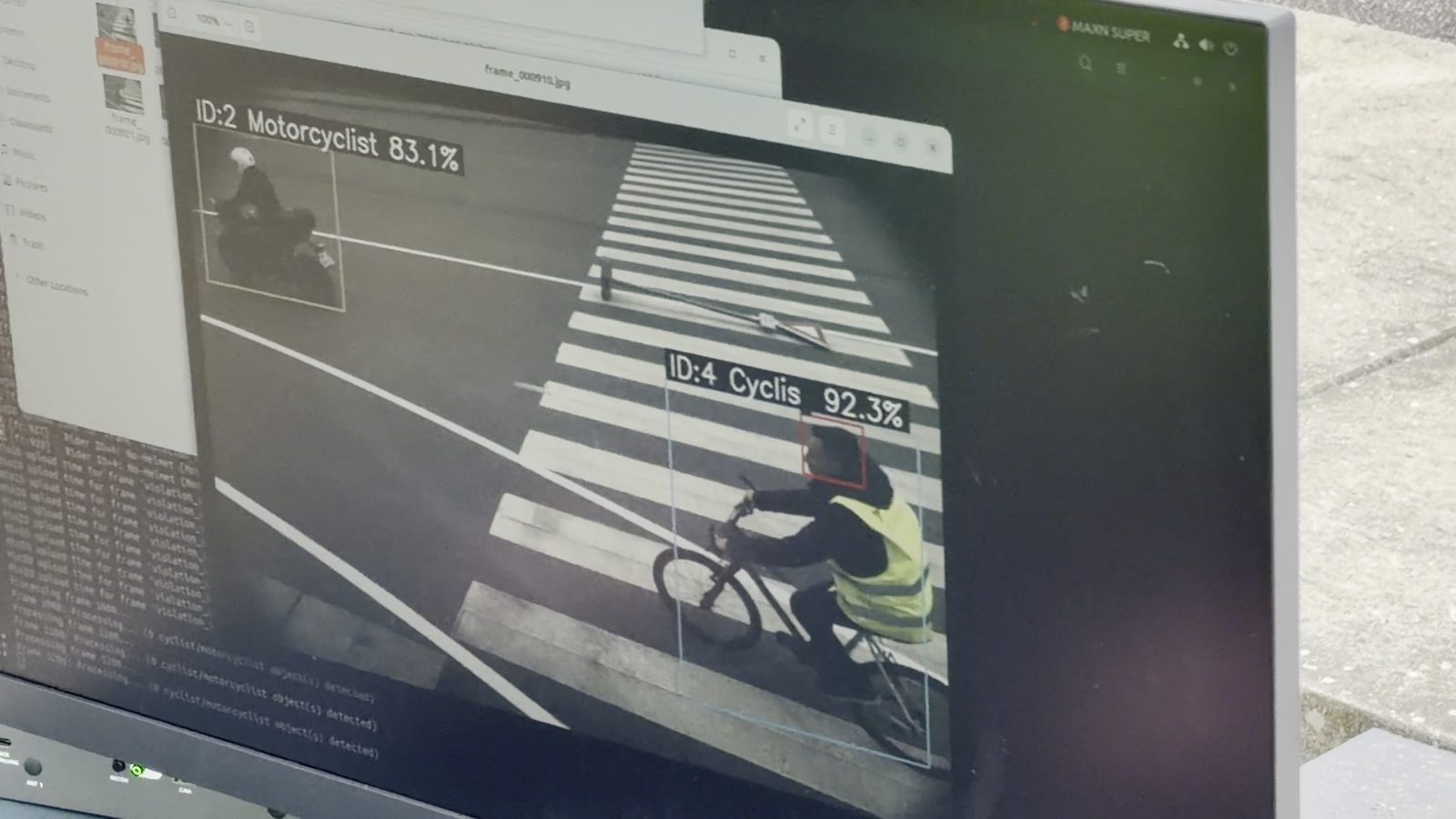 A monitor shows the iDriving AI model detecting and labelling a cyclist and a motorcyclist at the zebra crossing